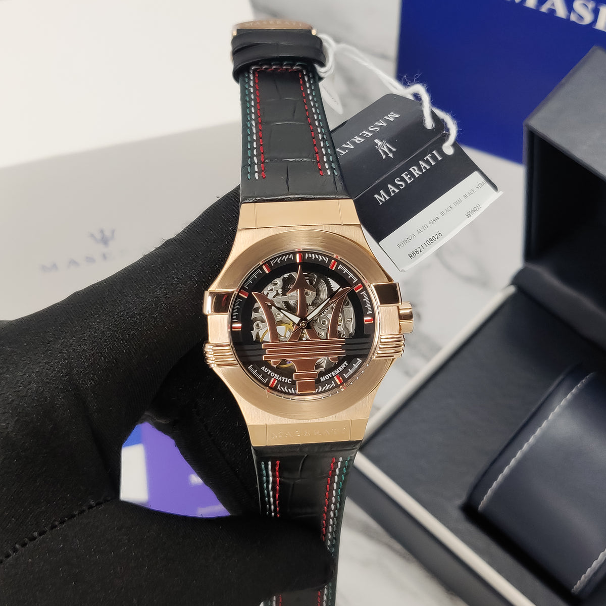 Luxury watch with black leather strap and gold case, displayed against a Maserati branded box.