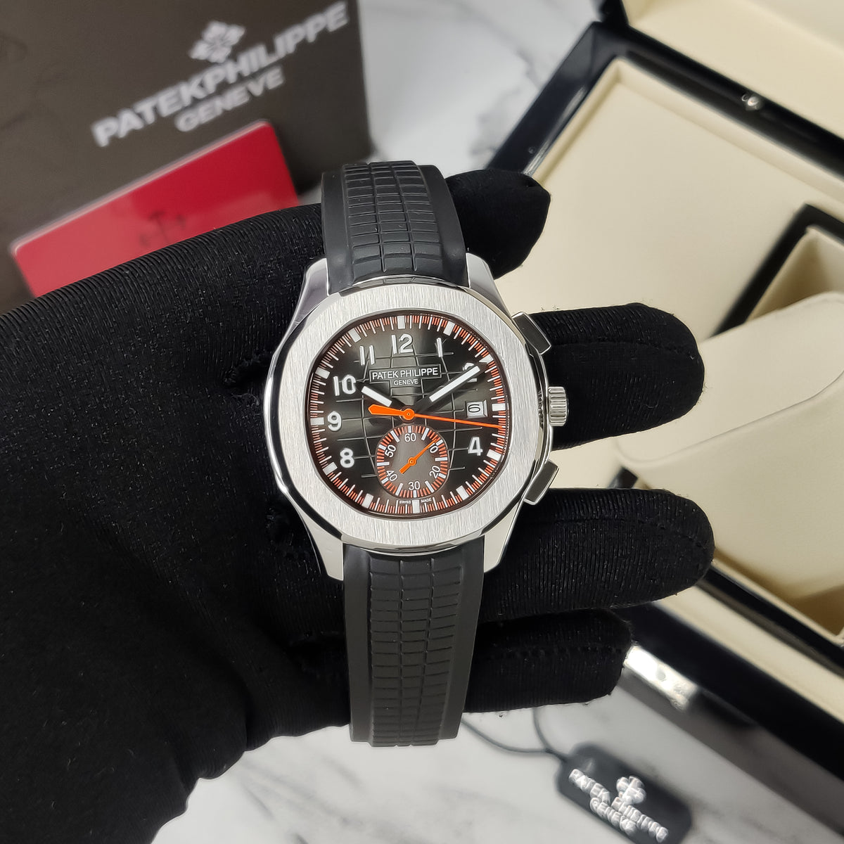 Patek Philippe watch held by a gloved hand with a branded box in the background